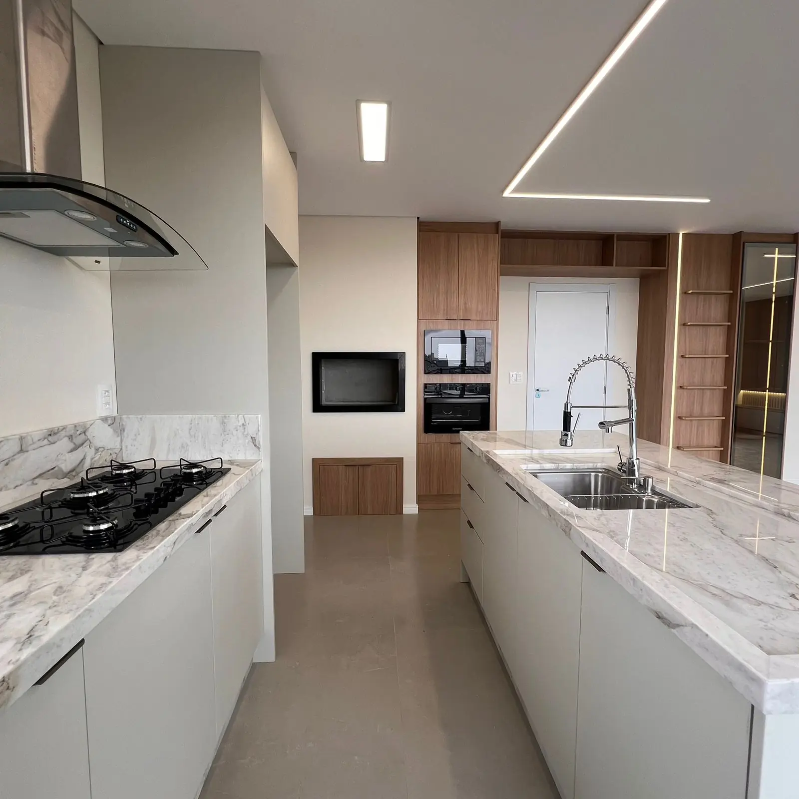 Cozinha planejada com cooktop, coifa e bancada de mármore em projeto DOMOV