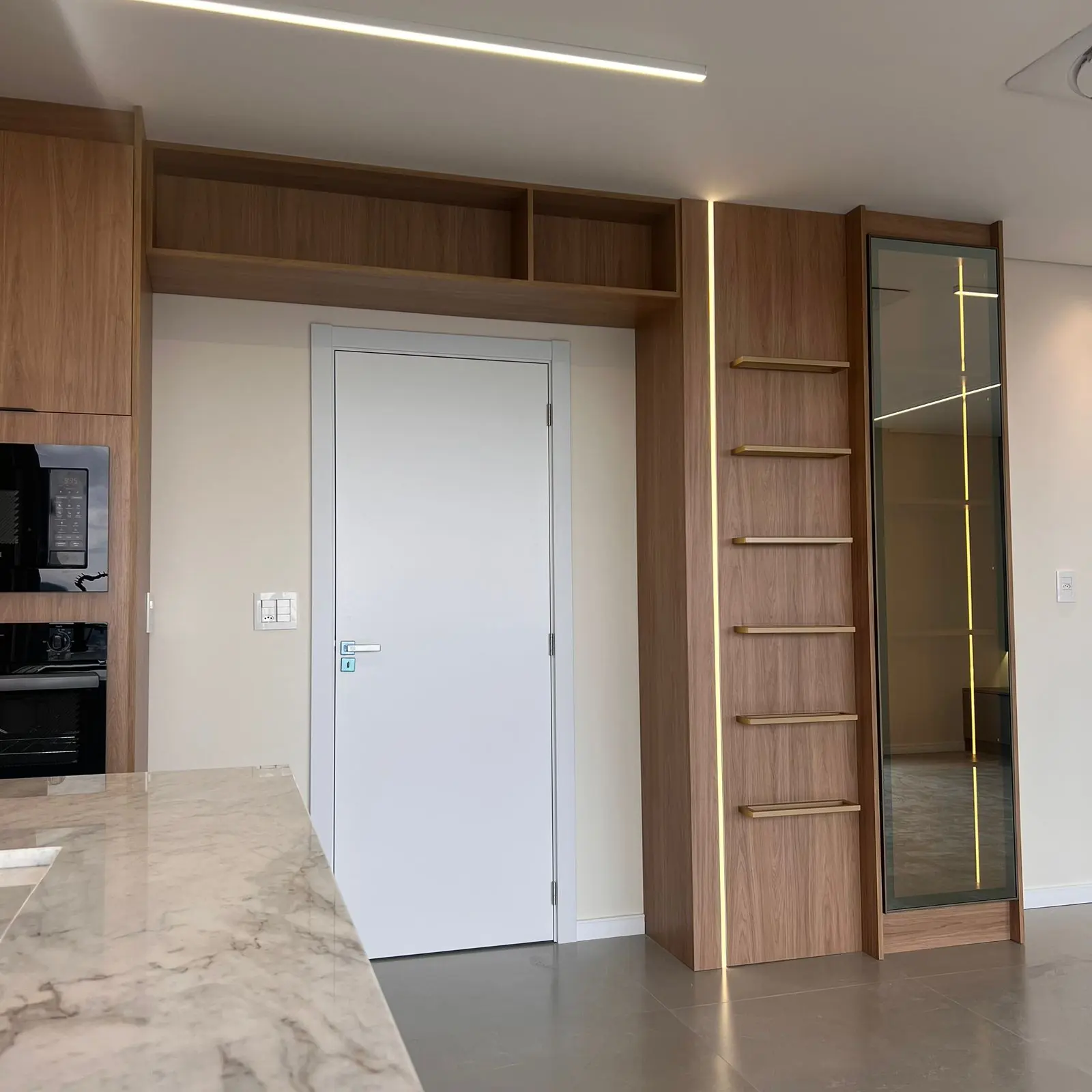Bancada de mármore branco com veios marcados e marcenaria amadeirada ao fundo