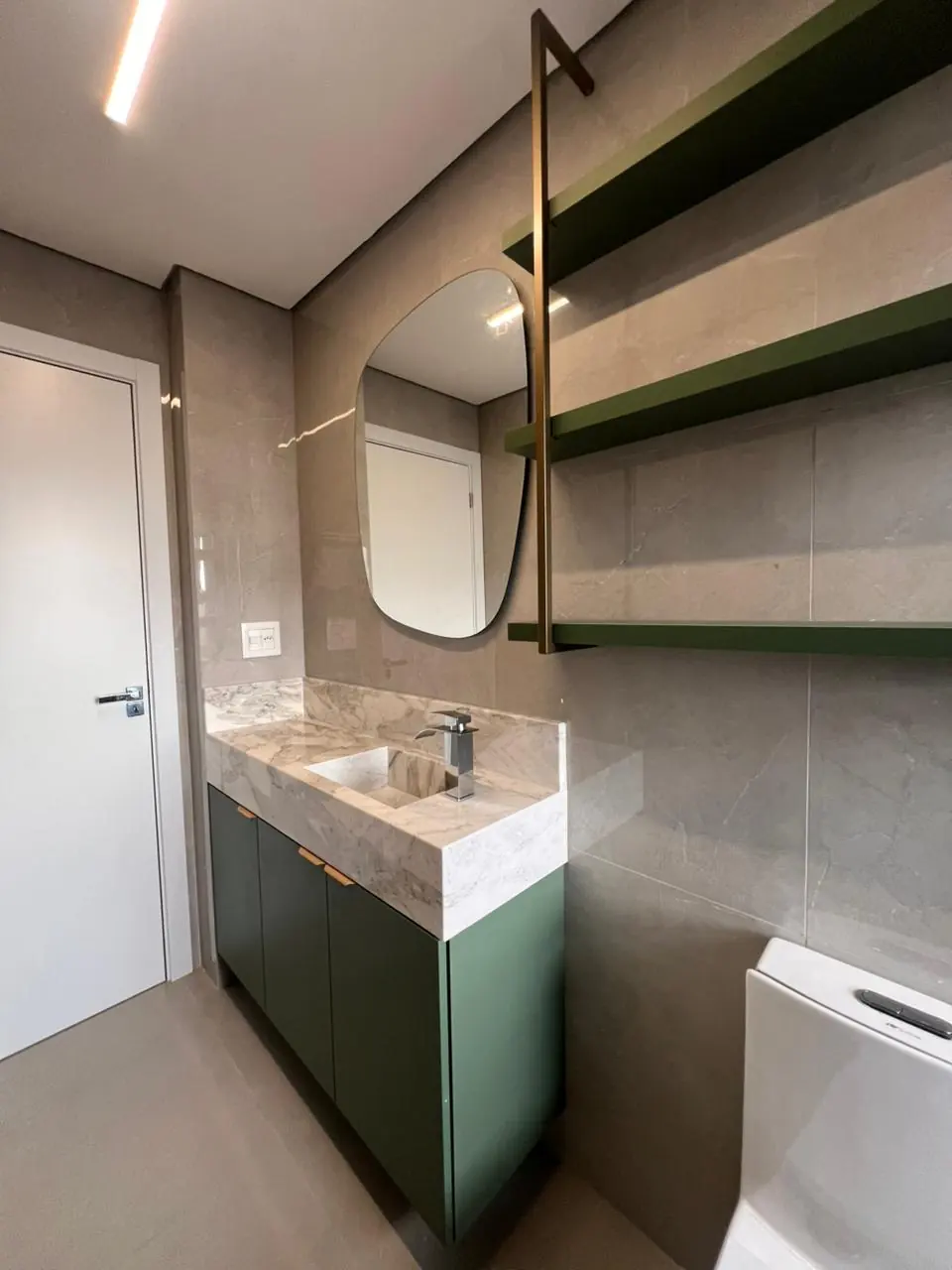 Lavabo com marcenaria verde profunda, cuba branca e detalhes em metal dourado