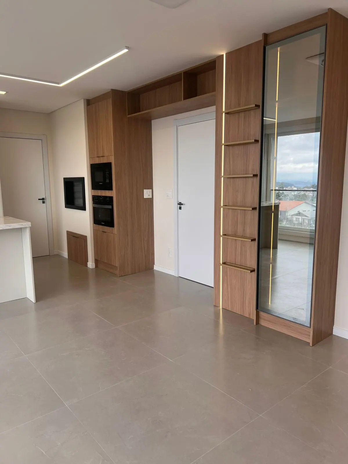 Living integrado com painel amadeirado, portas de vidro canelado e iluminação linear